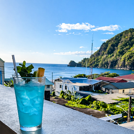 Refreshing blue cocktail with mint and pineapple garnish overlooking the Caribbean Sea and Soufrière coastline from Felicity Rooftop Restaurant, showcasing the best rooftop dining experience in Soufrière St Lucia.